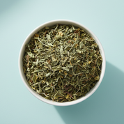 AzielCo. dried organic spearmint tea in a white bowl with a pale duck egg blue background